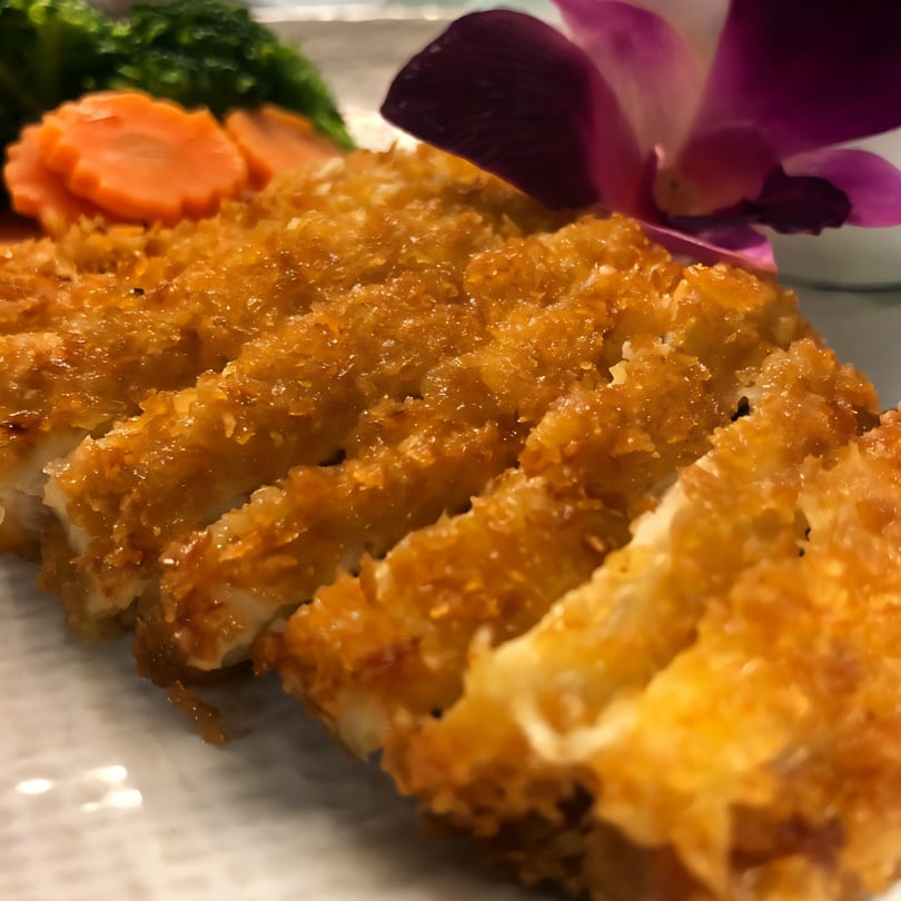 Crispy golden-brown chicken katsu slices, garnished with carved carrots, broccoli, and a purple orchid.