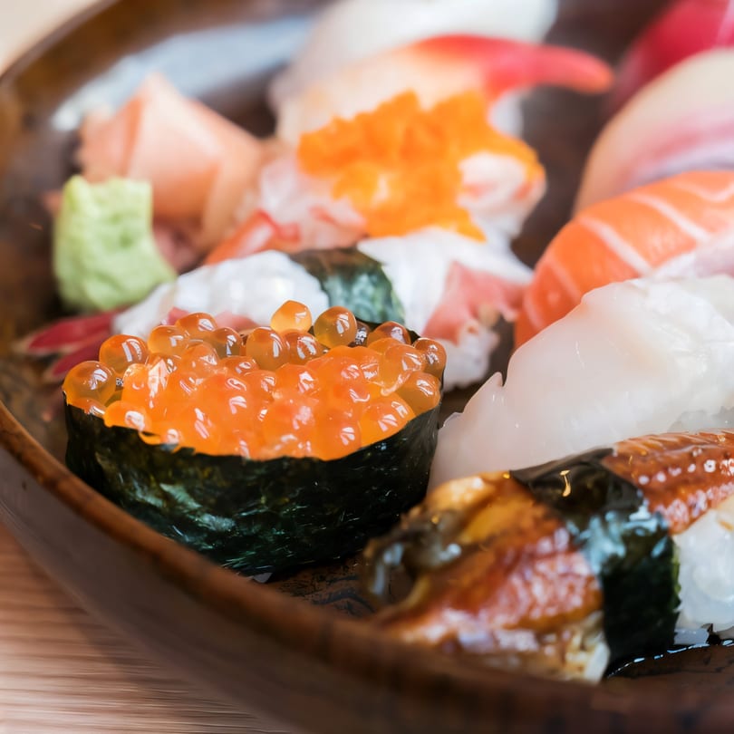 Close-up of a variety of colorful sushi and sashimi on a dark plate, including salmon roe.
