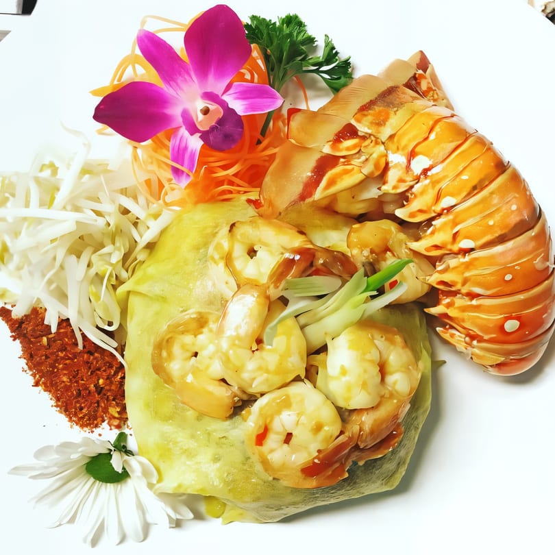 Japanese dish with shrimp, lobster tail, shredded cabbage, carrots, and an orchid garnish.